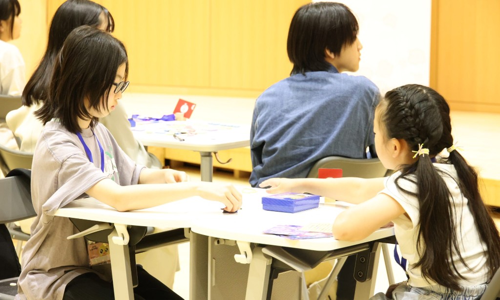 教材のコマやカードを使い、子どもたちが白いテーブルで集中して取り組んでいる様子