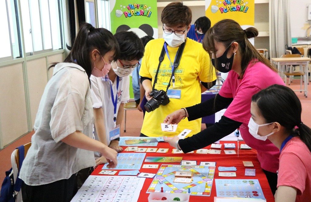 スタートアップポップコーンのボードゲーム教材を囲み、学ぶ子どもたちとファシリテーターの様子