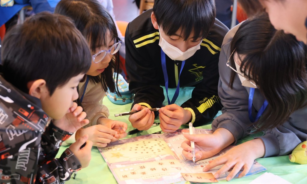 「輝く未来を描け!隠されたM&Aの秘密」の謎解きに、子どもたちがテーブルを囲んで協力して取り組む様子